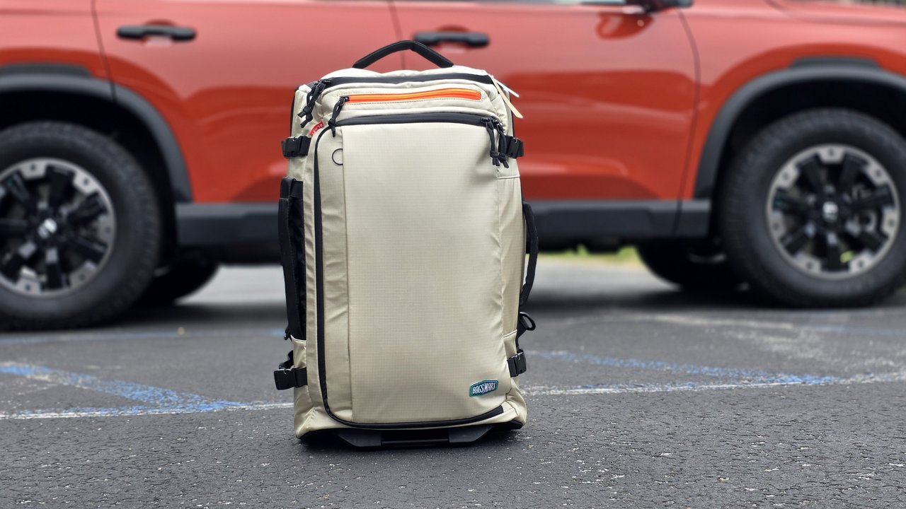 BagSmart Blast 43L Roller Backpack standing upright in a parking lot in front of an SUV