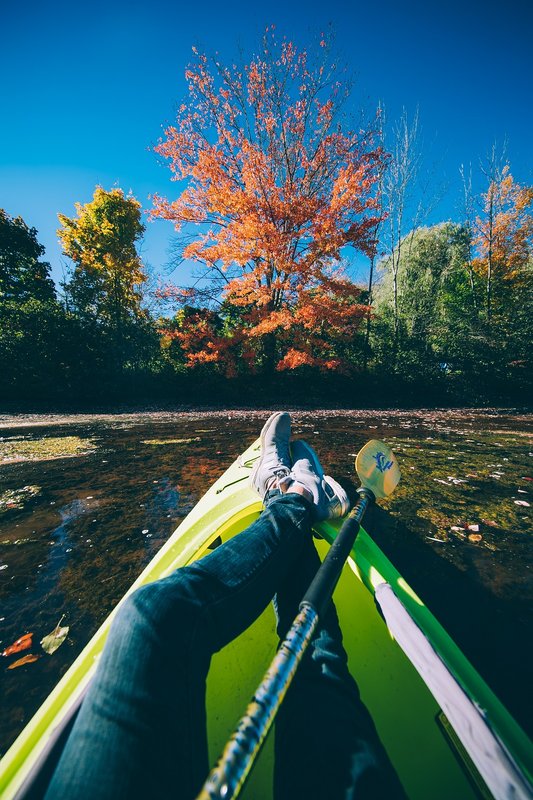 Kayaker's feet propped up on a green kayak facing a bright orange maple on the shore of Lake Wawaka