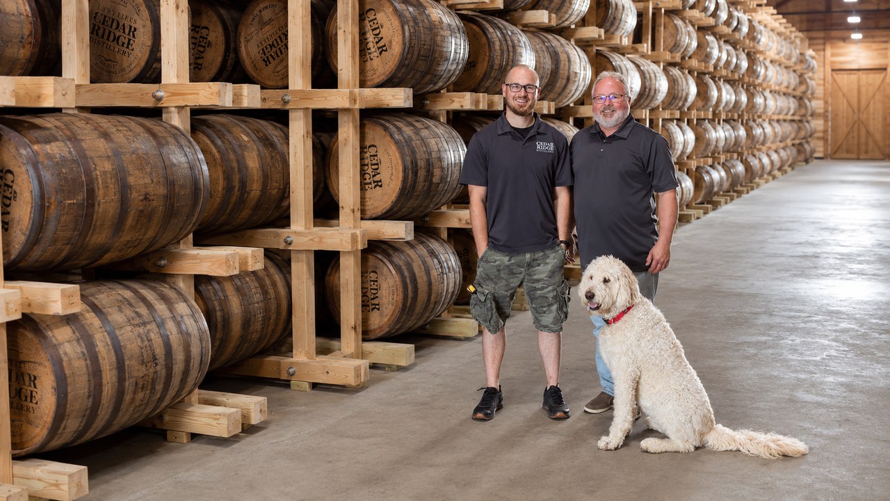 A father and son with their dog among the whiskey barrels in the rickhouse at Cedar Ridge Distillery in Iowa