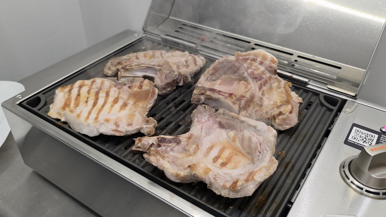 Four bone-in pork chops searing with grill marks on the Kenyon City Grill