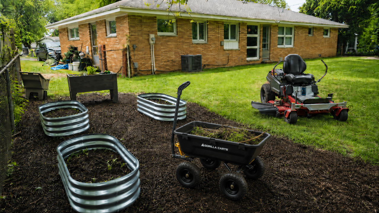 Backyard spring cleanup scene with galvanized raised beds, wood planter box, dump cart full of yard debris, and red zero-turn riding mower on a freshly mulched and cleaned lawn