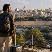 A traveler with a backpack and two suitcases looking out over the Old City of Jerusalem