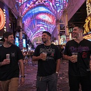 Three guys laughing on Fremont Street under the canopy holding drinks during a Vegas guys trip