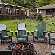 Fire pit ringed with green Adirondack chairs at Hemlock, the adult summer camp resort in the Catskills