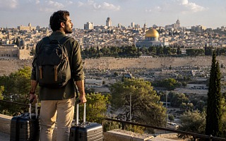 A traveler with a backpack and two suitcases looking out over the Old City of Jerusalem